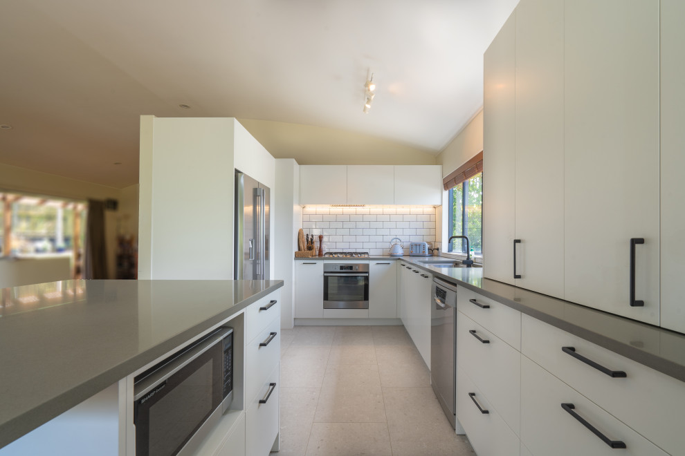 Contemporary galley kitchen/diner in Auckland with white cabinets, engineered stone countertops, metro tiled splashback, stainless steel appliances, laminate floors, an island, grey floors and grey worktops.