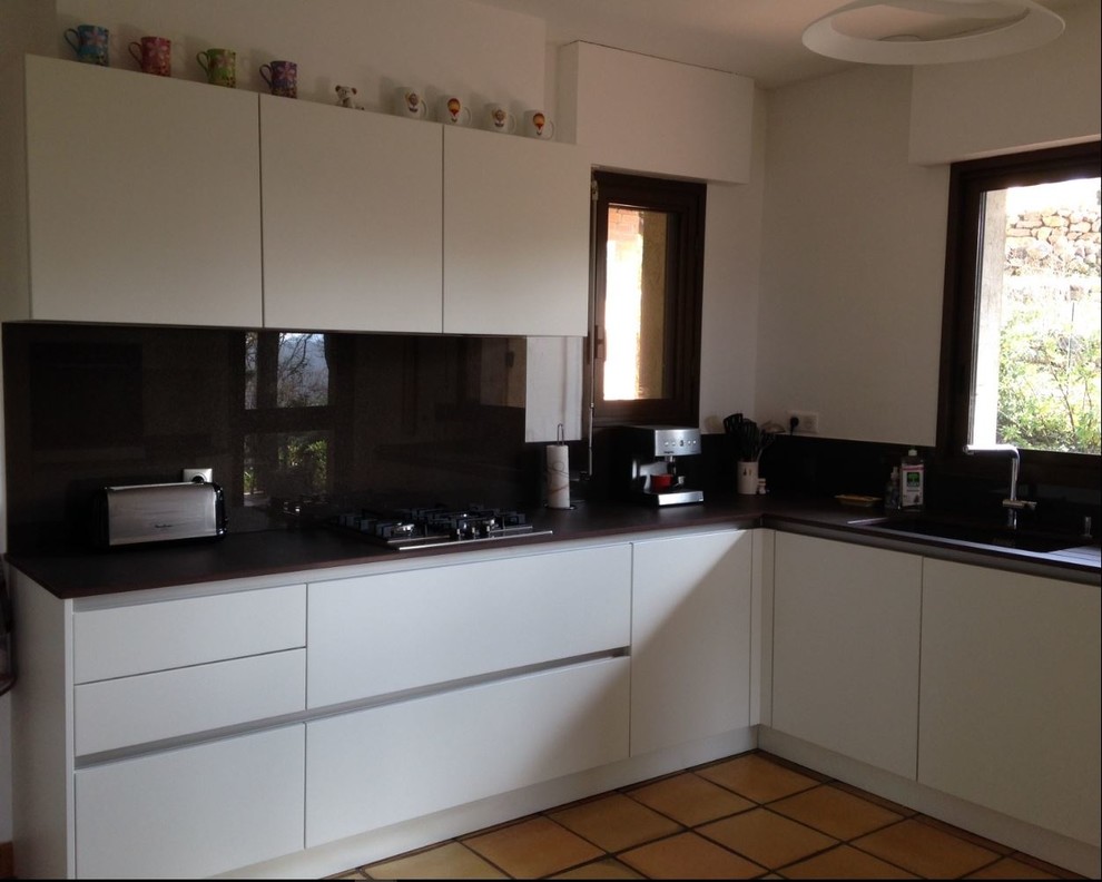 This is an example of a medium sized contemporary l-shaped open plan kitchen in Toulouse with an integrated sink, beaded cabinets, stainless steel cabinets, quartz worktops, black splashback, glass tiled splashback, coloured appliances, ceramic flooring, an island, brown floors and black worktops.