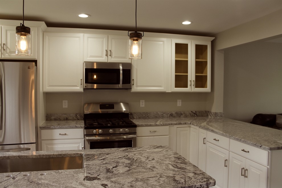 This is an example of a mid-sized arts and crafts l-shaped open plan kitchen in Detroit with white cabinets, granite benchtops, an undermount sink, raised-panel cabinets, beige splashback, stainless steel appliances and multiple islands.