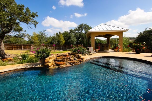 Large eclectic backyard custom-shaped natural pool in Austin with a water feature and stamped concrete.