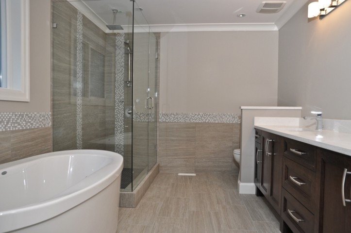 Mid-sized transitional master bathroom in Vancouver with recessed-panel cabinets, dark wood cabinets, a freestanding tub, a corner shower, a two-piece toilet, beige tile, gray tile, white tile, porcelain tile, beige walls, porcelain floors, an undermount sink, engineered quartz benchtops, beige floor, a hinged shower door and white benchtops.