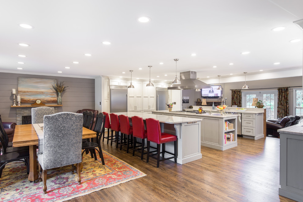 Large transitional single-wall medium tone wood floor and brown floor eat-in kitchen photo with an undermount sink, shaker cabinets, white cabinets, marble countertops, multicolored backsplash, matchstick tile backsplash, stainless steel appliances and two islands