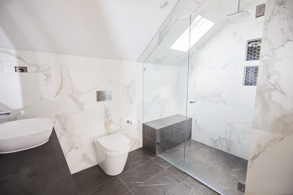 This is an example of a mid-sized contemporary master bathroom in Sydney with an alcove shower, a two-piece toilet, multi-coloured tile, multi-coloured walls, a console sink, multi-coloured floor, a hinged shower door, black benchtops, a freestanding tub, marble and marble floors.