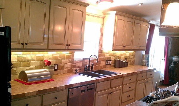 Mountain style single-wall medium tone wood floor eat-in kitchen photo in Austin with raised-panel cabinets, distressed cabinets, laminate countertops, multicolored backsplash, stone tile backsplash, stainless steel appliances, an island and a double-bowl sink