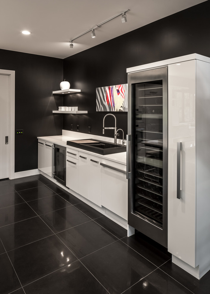 Photo of an expansive contemporary single-wall home bar in Minneapolis with a drop-in sink, flat-panel cabinets, white cabinets, quartz benchtops, white splashback, porcelain floors and black floor.