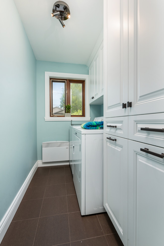 Photo of a small traditional single-wall utility room in Montreal with raised-panel cabinets, white cabinets, blue walls, ceramic floors, a side-by-side washer and dryer and brown floor.