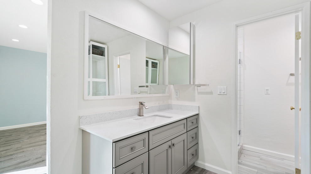 This is an example of a mid-sized transitional 3/4 bathroom in San Francisco with recessed-panel cabinets, grey cabinets, a corner shower, white tile, subway tile, grey walls, porcelain floors, an undermount sink, engineered quartz benchtops, grey floor, a hinged shower door and white benchtops.