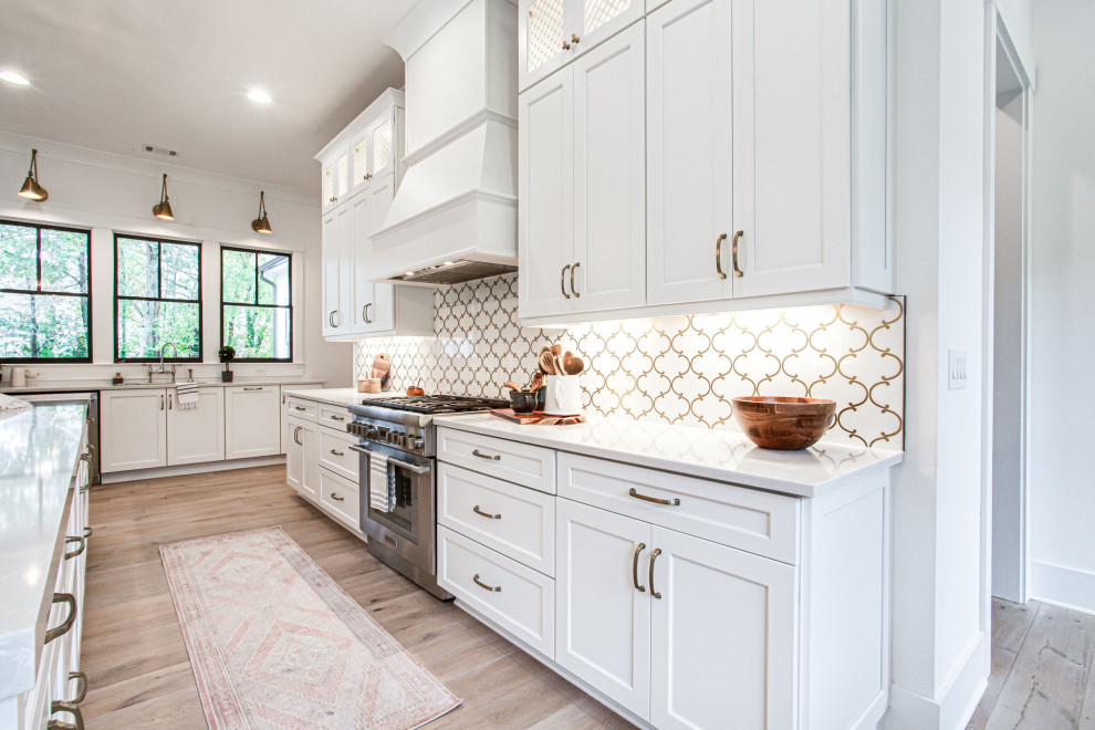 Photo of a large country u-shaped open plan kitchen in Atlanta with a farmhouse sink, shaker cabinets, white cabinets, quartz benchtops, white splashback, mosaic tile splashback, stainless steel appliances, light hardwood floors, with island, beige floor, grey benchtop and vaulted.
