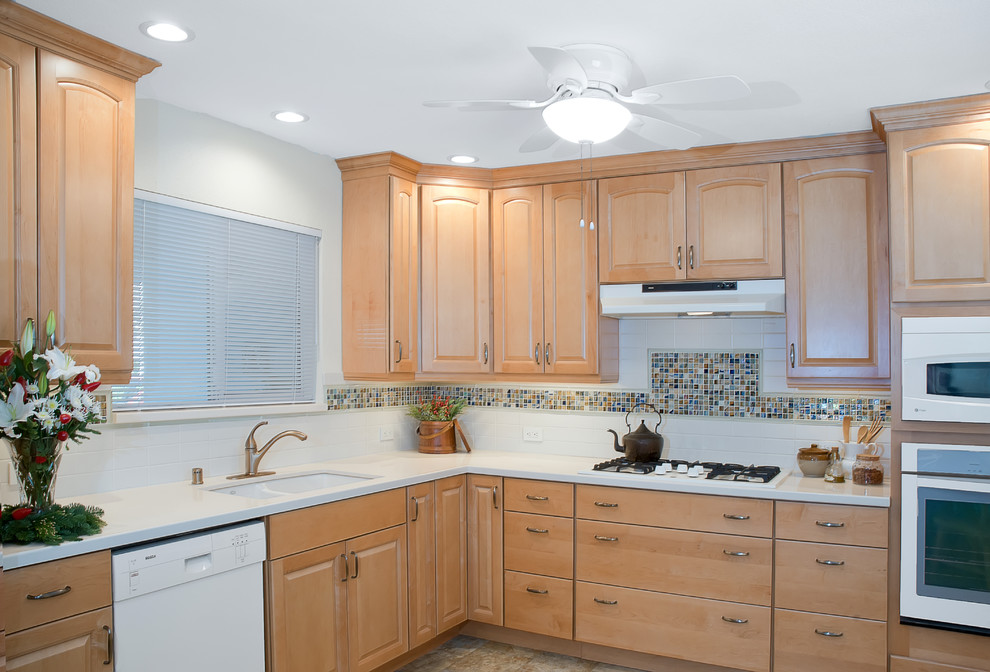 This is an example of a mid-sized transitional l-shaped eat-in kitchen in San Diego with an undermount sink, raised-panel cabinets, light wood cabinets, quartz benchtops, multi-coloured splashback, subway tile splashback, white appliances and no island.