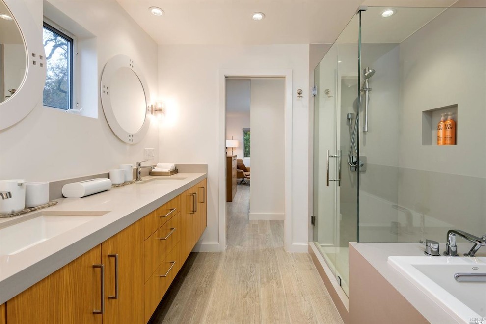 This is an example of a mid-sized contemporary master bathroom in San Francisco with flat-panel cabinets, medium wood cabinets, a drop-in tub, an alcove shower, a one-piece toilet, gray tile, white walls, porcelain floors, an undermount sink and solid surface benchtops.