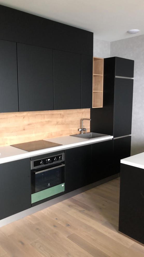 Mid-sized contemporary single-wall eat-in kitchen in Other with an undermount sink, flat-panel cabinets, black cabinets, laminate benchtops, beige splashback, timber splashback, black appliances, medium hardwood floors, multiple islands, beige floor and white benchtop.