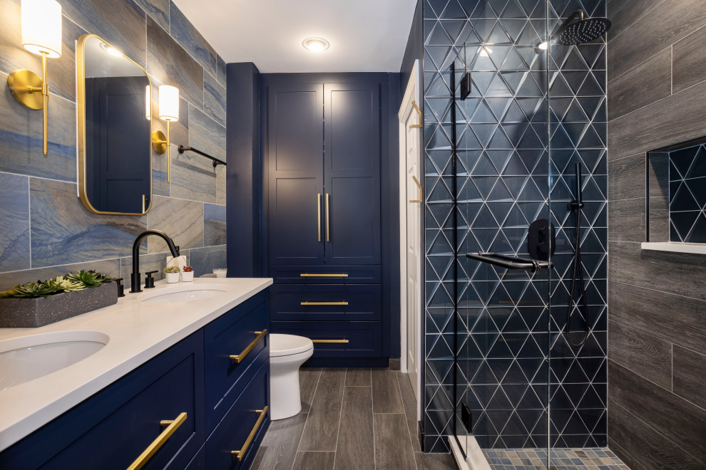 This is an example of a mid-sized modern master bathroom in Chicago with grey floor, blue cabinets, a double vanity, blue walls, wood-look tile, shaker cabinets, an alcove shower, a two-piece toilet, gray tile, wood-look tile, an undermount sink, a niche, a built-in vanity and white benchtops.