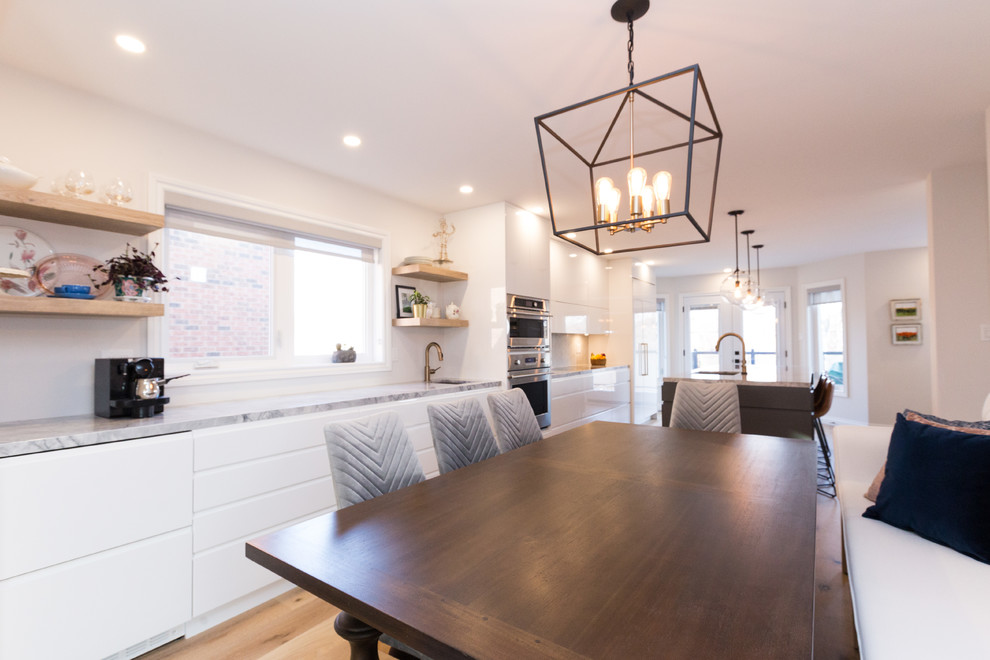 Large modern single-wall eat-in kitchen in Toronto with an undermount sink, flat-panel cabinets, white cabinets, quartzite benchtops, white splashback, marble splashback, stainless steel appliances, light hardwood floors, with island and beige floor.