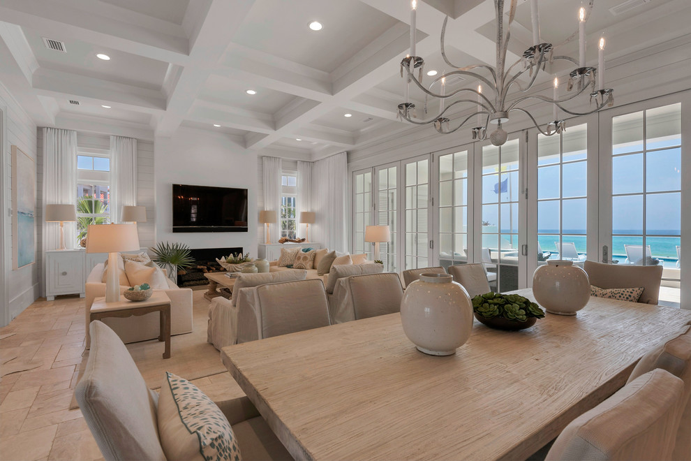 This is an example of an expansive beach style dining room in Miami with white walls, travertine floors, a standard fireplace and a tile fireplace surround.