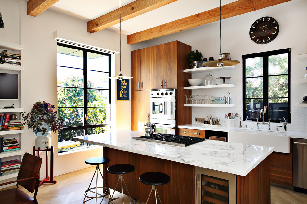 Design ideas for a mid-sized contemporary galley eat-in kitchen in Los Angeles with flat-panel cabinets, dark wood cabinets, white splashback, medium hardwood floors, with island, brown floor, a farmhouse sink, marble benchtops, subway tile splashback and stainless steel appliances.