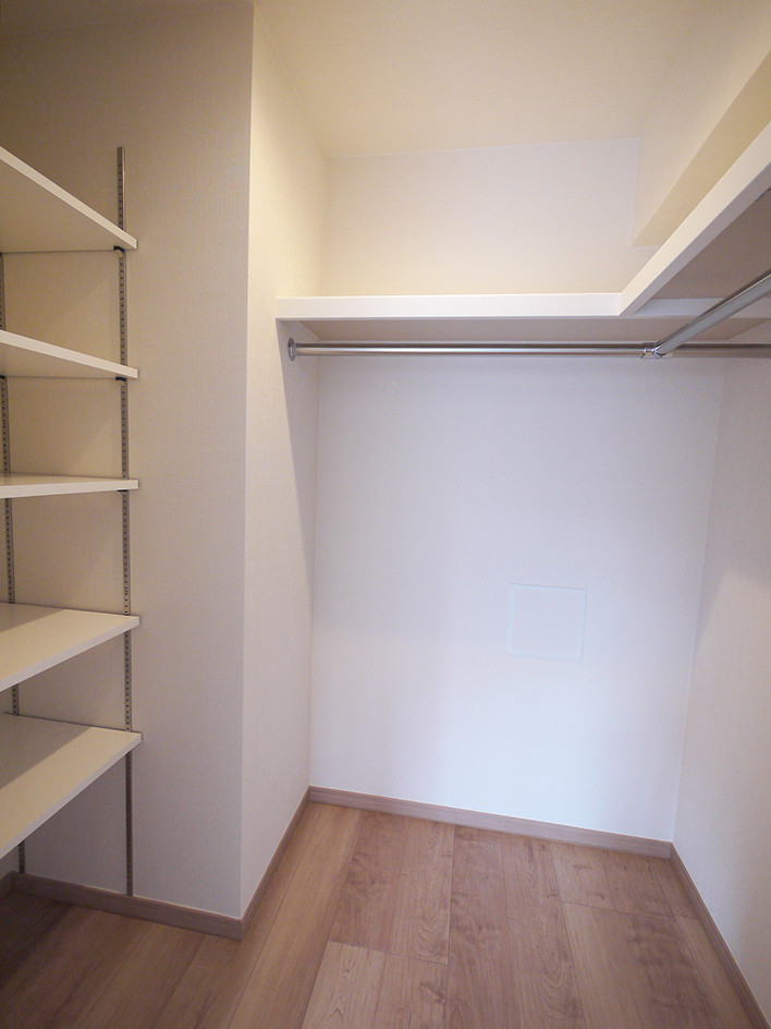 Scandinavian walk-in wardrobe in Tokyo with white cabinets, plywood floors and beige floor.