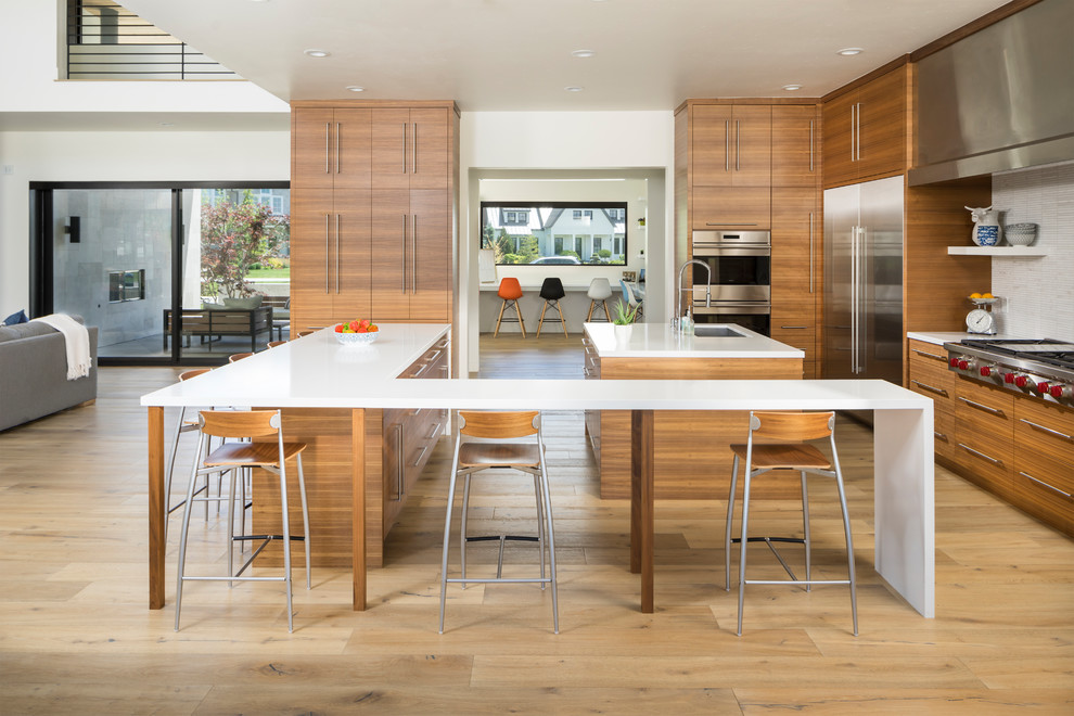 Expansive contemporary u-shaped open plan kitchen in Salt Lake City with an undermount sink, flat-panel cabinets, medium wood cabinets, white splashback, stainless steel appliances, light hardwood floors, with island, beige floor and white benchtop.