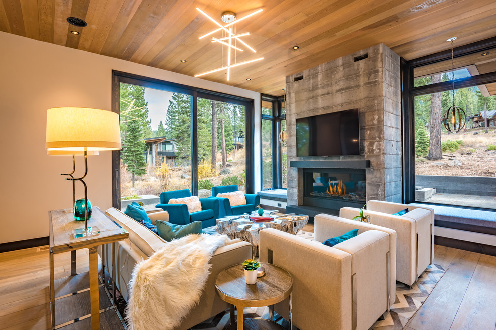Large modern open concept living room with grey walls, medium hardwood floors, a standard fireplace, a concrete fireplace surround, a wall-mounted tv, brown floor and wood.