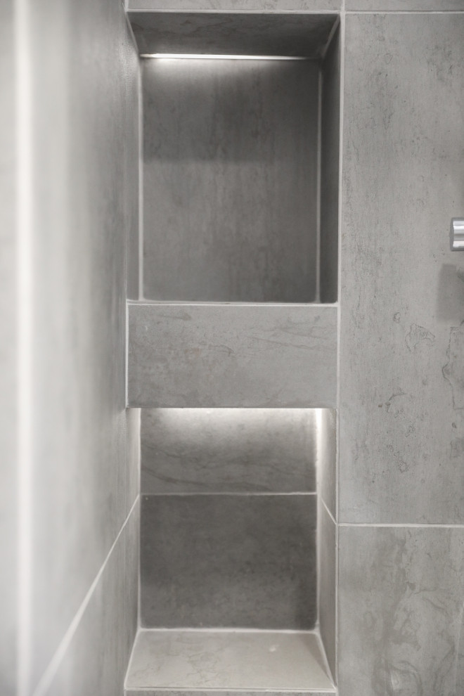 Modern inredning av ett mellanstort vit vitt badrum med dusch, med släta luckor, skåp i mellenmörkt trä, en dusch i en alkov, en vägghängd toalettstol, grå kakel, stenkakel, grå väggar, klinkergolv i keramik, ett nedsänkt handfat, bänkskiva i akrylsten, grått golv och med dusch som är öppen
