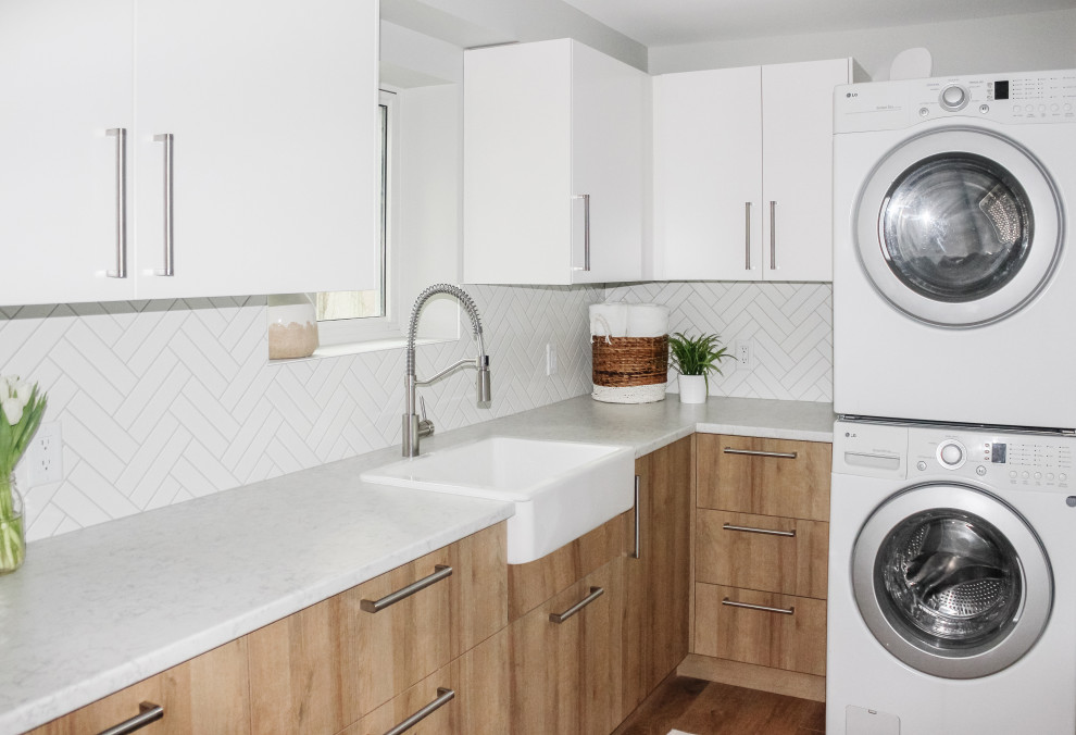 This is an example of a mid-sized modern l-shaped utility room in Vancouver with a farmhouse sink, flat-panel cabinets, light wood cabinets, laminate benchtops, white splashback, ceramic splashback, grey walls, vinyl floors, a stacked washer and dryer and white benchtop.
