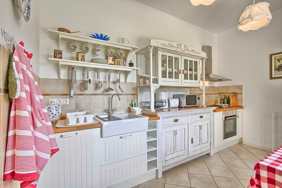 Inspiration for a mid-sized country single-wall eat-in kitchen in Other with a farmhouse sink, white cabinets, wood benchtops, stainless steel appliances, terra-cotta floors and beige splashback.
