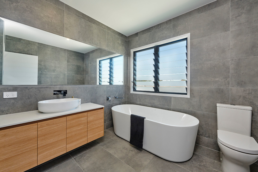 Photo of a contemporary master bathroom in Brisbane with flat-panel cabinets, medium wood cabinets, a freestanding tub, a one-piece toilet, gray tile, grey walls, a vessel sink, grey floor and white benchtops.