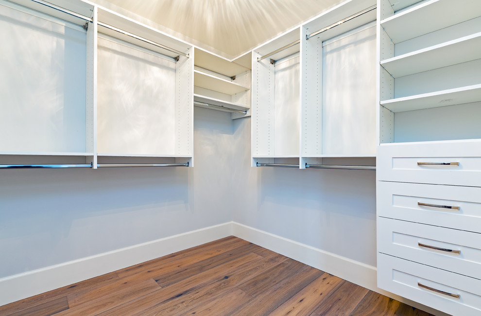 Example of a mid-sized transitional gender-neutral medium tone wood floor walk-in closet design with shaker cabinets and white cabinets