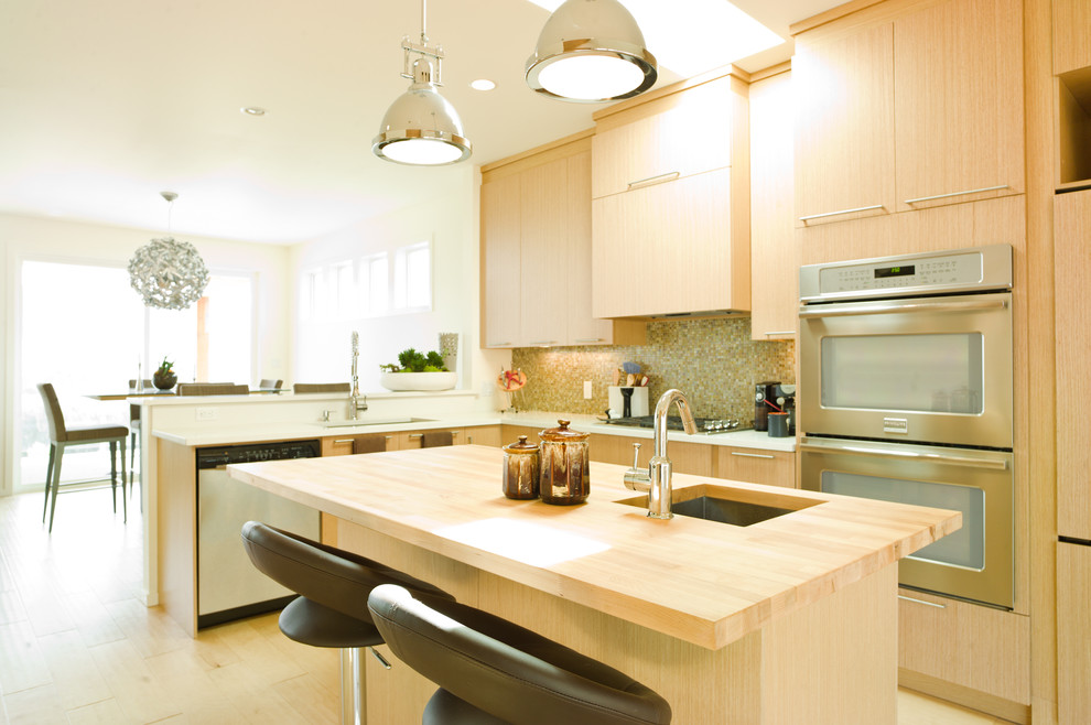 Photo of a modern kitchen in Vancouver with mosaic tile splashback, wood benchtops, flat-panel cabinets, light wood cabinets, an undermount sink, green splashback and stainless steel appliances.