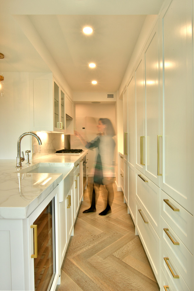Photo of a small transitional galley eat-in kitchen in New York with an undermount sink, shaker cabinets, white cabinets, marble benchtops, white splashback, stone slab splashback, panelled appliances, light hardwood floors, with island, beige floor and white benchtop.