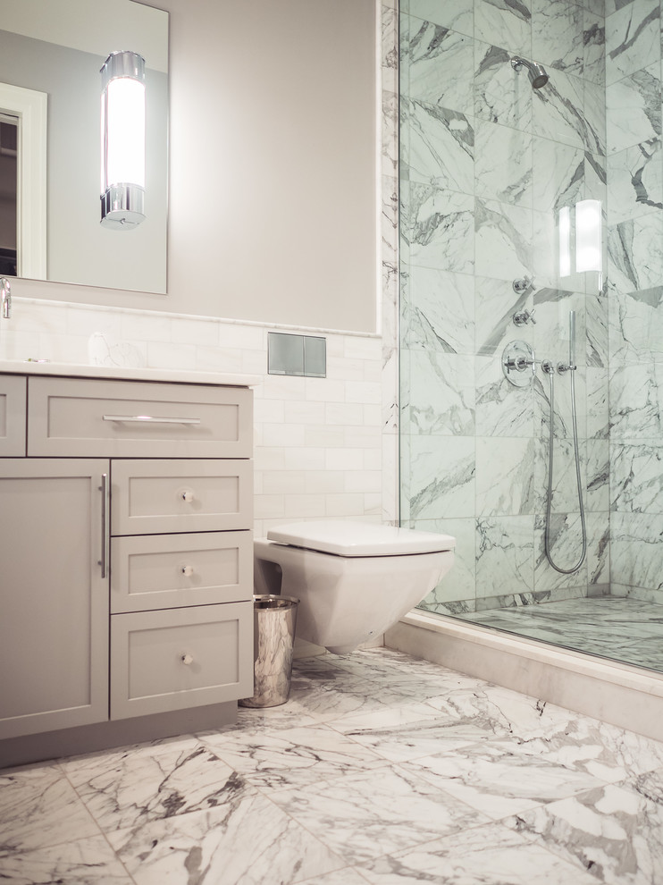 Photo of a mid-sized contemporary master bathroom in New York with shaker cabinets, grey cabinets, white tile, subway tile, solid surface benchtops, an alcove shower, a wall-mount toilet, grey walls, marble floors and an undermount sink.
