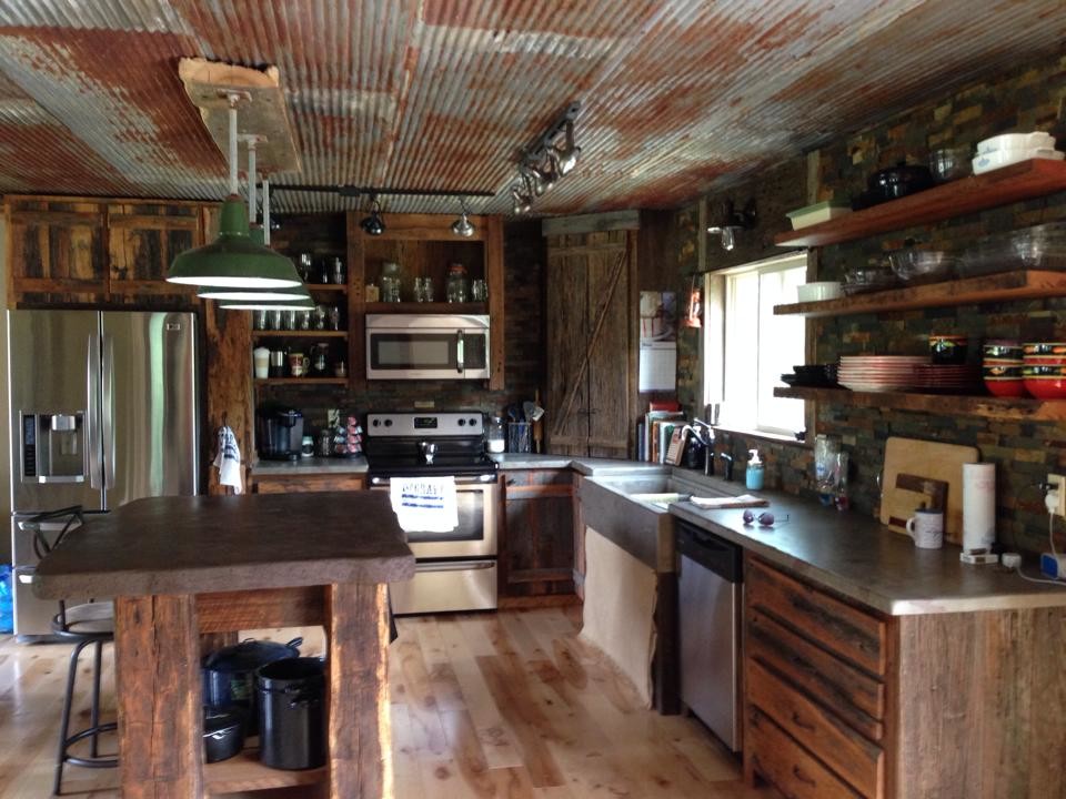 Mid-sized country l-shaped eat-in kitchen in Nashville with a farmhouse sink, flat-panel cabinets, distressed cabinets, concrete benchtops, stainless steel appliances, light hardwood floors and with island.