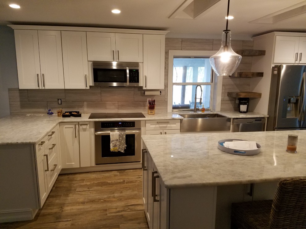 Large beach style l-shaped eat-in kitchen in Other with a farmhouse sink, shaker cabinets, white cabinets, granite benchtops, grey splashback, ceramic splashback, stainless steel appliances, ceramic floors and with island.