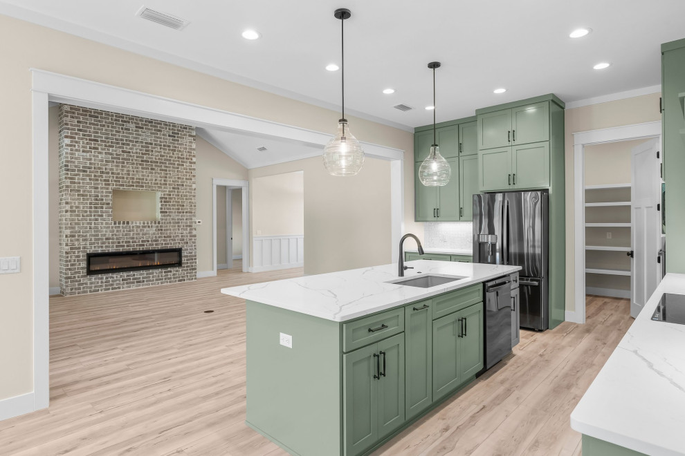 Arts and crafts l-shaped vinyl floor and beige floor open concept kitchen photo with an undermount sink, shaker cabinets, green cabinets, quartzite countertops, beige backsplash, porcelain backsplash, stainless steel appliances, an island and white countertops