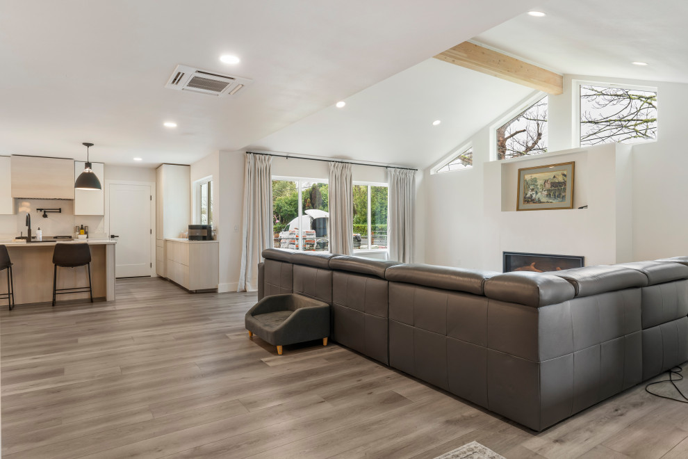 This is an example of a mid-sized modern formal open concept living room in Seattle with white walls, vinyl floors, a standard fireplace, a plaster fireplace surround, a wall-mounted tv, brown floor and vaulted.