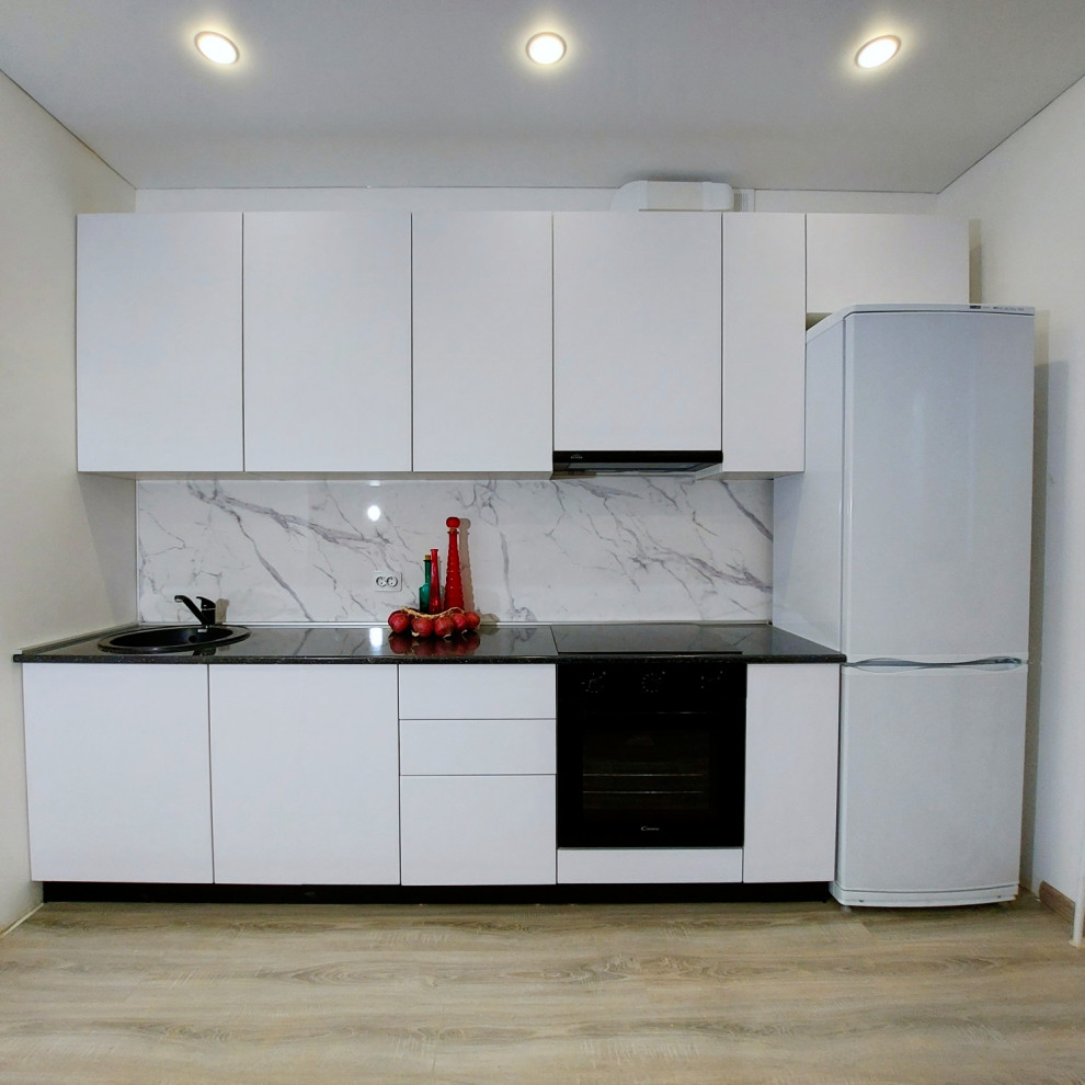 Mid-sized transitional single-wall separate kitchen in Other with an undermount sink, flat-panel cabinets, white cabinets, solid surface benchtops, white splashback, porcelain splashback, black appliances, light hardwood floors, no island, beige floor, black benchtop and recessed.