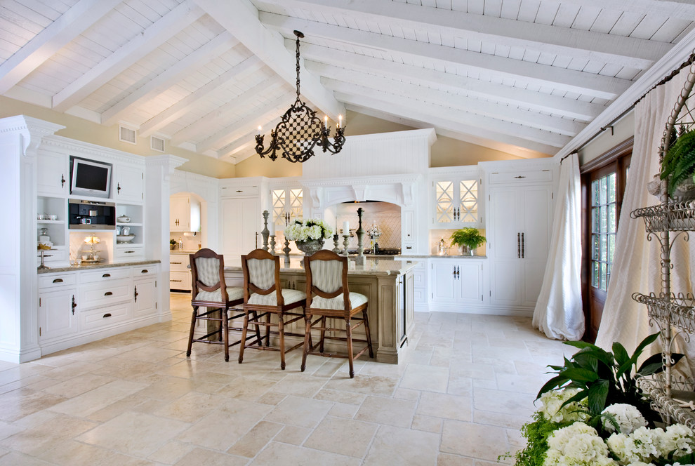 Photo of a mediterranean l-shaped kitchen in Orange County with raised-panel cabinets, white cabinets, white splashback, panelled appliances and with island.
