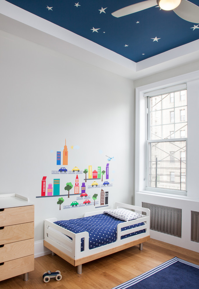 This is an example of a contemporary toddler room for boys in New York with white walls and medium hardwood floors.