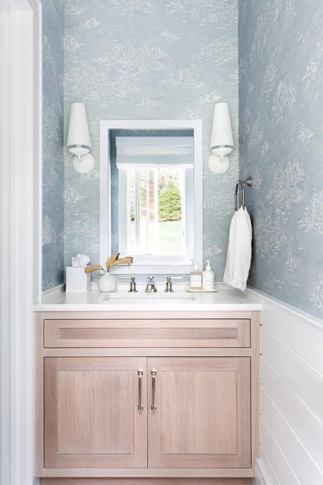 Mid-sized traditional powder room in New York with recessed-panel cabinets, light wood cabinets, a one-piece toilet, grey walls, light hardwood floors, an integrated sink, marble benchtops, brown floor and white benchtops.