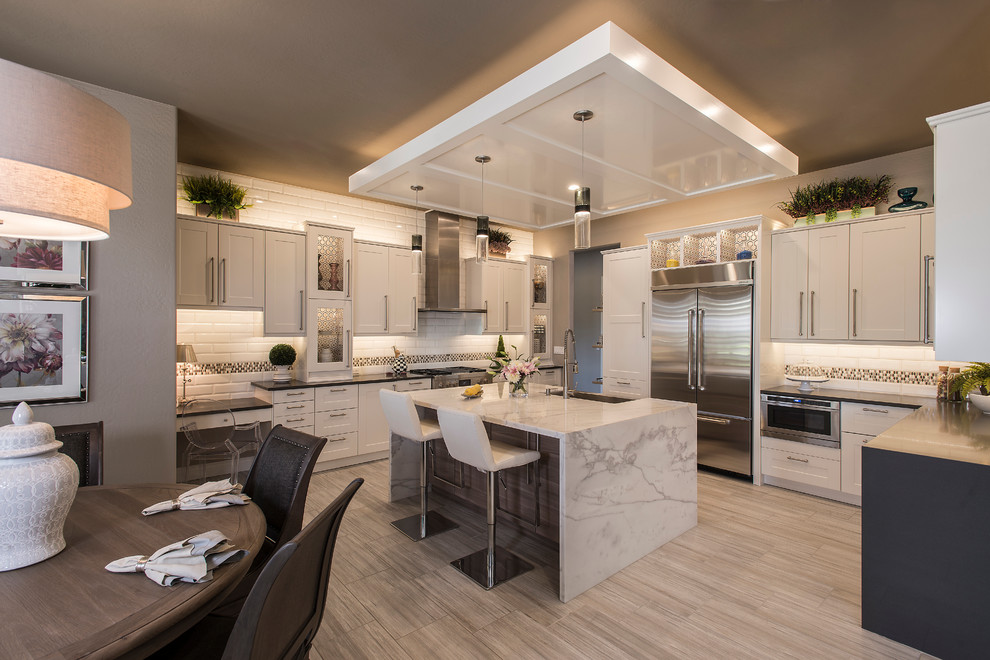 Open concept kitchen - mid-sized transitional u-shaped porcelain tile open concept kitchen idea in Phoenix with a farmhouse sink, shaker cabinets, white cabinets, solid surface countertops, white backsplash, subway tile backsplash, stainless steel appliances and an island
