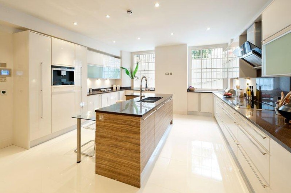 Photo of a large modern u-shaped kitchen in London with a double-bowl sink, flat-panel cabinets, stainless steel appliances, with island, white floor, black benchtop and white cabinets.