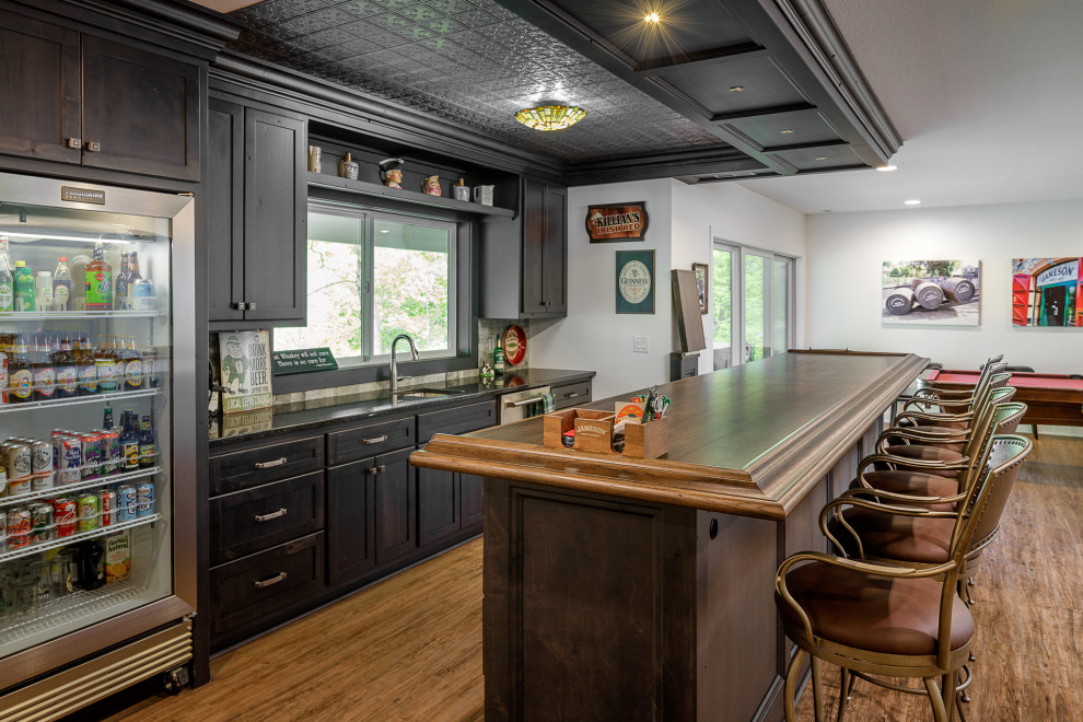 Photo of a traditional galley seated home bar in Other with an undermount sink, shaker cabinets, dark wood cabinets, medium hardwood floors, brown floor and black benchtop.