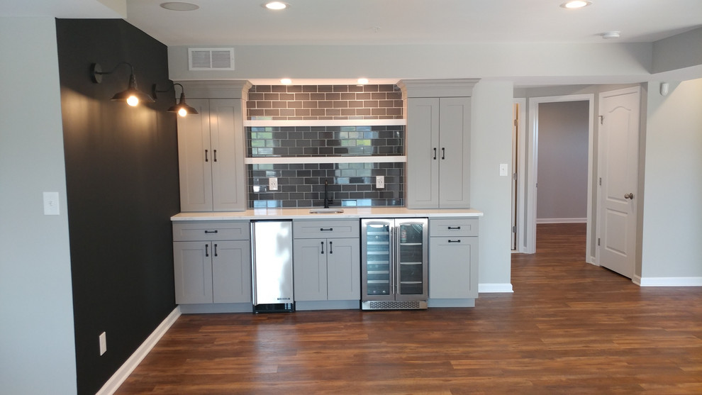 Inspiration for a traditional l-shaped home bar in Baltimore with an undermount sink, shaker cabinets, grey cabinets, marble benchtops, brown splashback, ceramic splashback, dark hardwood floors, brown floor and white benchtop.
