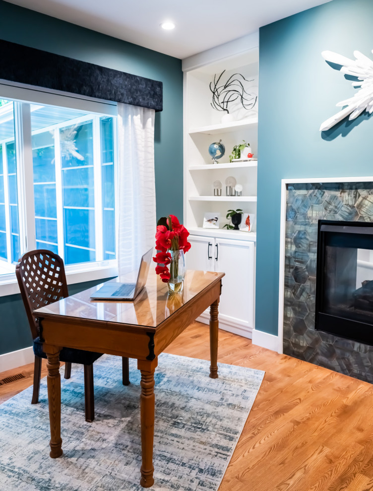 На фото: домашняя мастерская среднего размера в стиле модернизм с синими стенами, паркетным полом среднего тона, стандартным камином, отдельно стоящим рабочим столом, фасадом камина из плитки и коричневым полом с