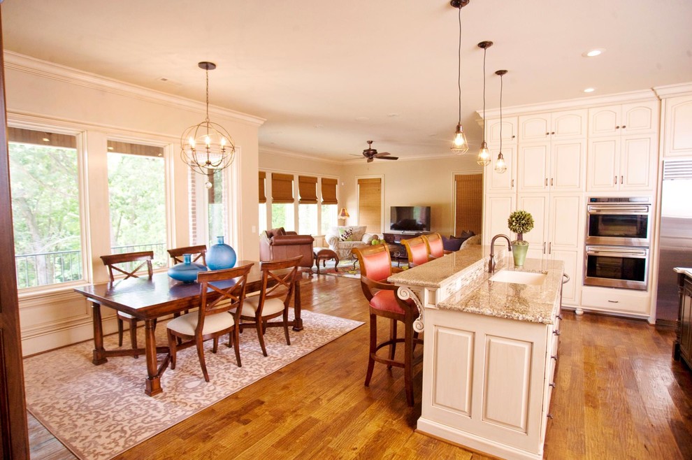 Example of a huge l-shaped medium tone wood floor eat-in kitchen design with an undermount sink, raised-panel cabinets, white cabinets, granite countertops, beige backsplash, stainless steel appliances and an island