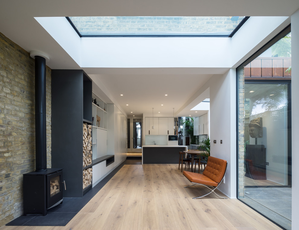 Photo of a mid-sized contemporary open concept living room in London with light hardwood floors, a wood stove, a brick fireplace surround and a concealed tv.