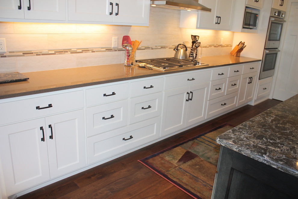 Example of a mid-sized transitional l-shaped dark wood floor open concept kitchen design with an undermount sink, recessed-panel cabinets, white cabinets, quartz countertops, beige backsplash, ceramic backsplash, stainless steel appliances and an island