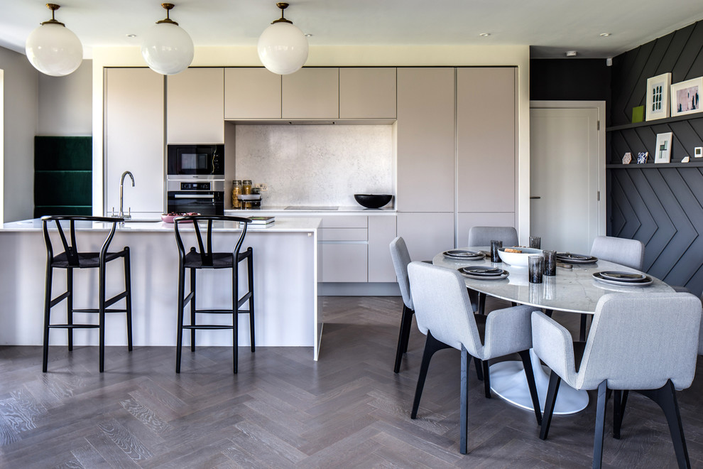 This is an example of a mid-sized contemporary galley eat-in kitchen in Dublin with medium hardwood floors, grey floor, flat-panel cabinets, grey cabinets, quartzite benchtops, with island, an undermount sink, grey splashback, panelled appliances and white benchtop.