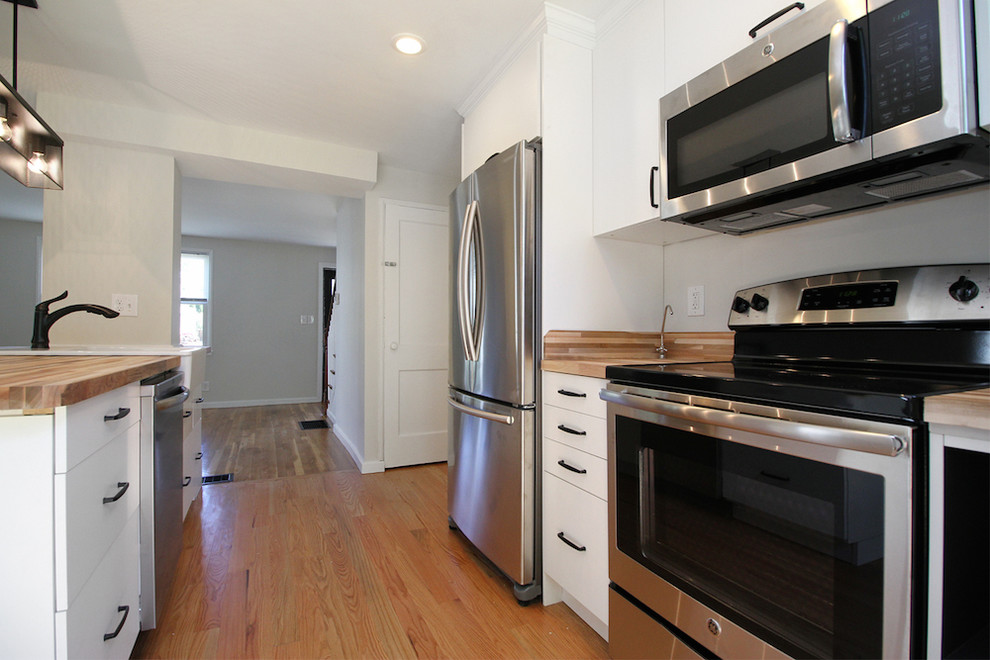 This is an example of a mid-sized modern galley open plan kitchen in Providence with a single-bowl sink, flat-panel cabinets, white cabinets, wood benchtops, white splashback, stainless steel appliances, medium hardwood floors and with island.