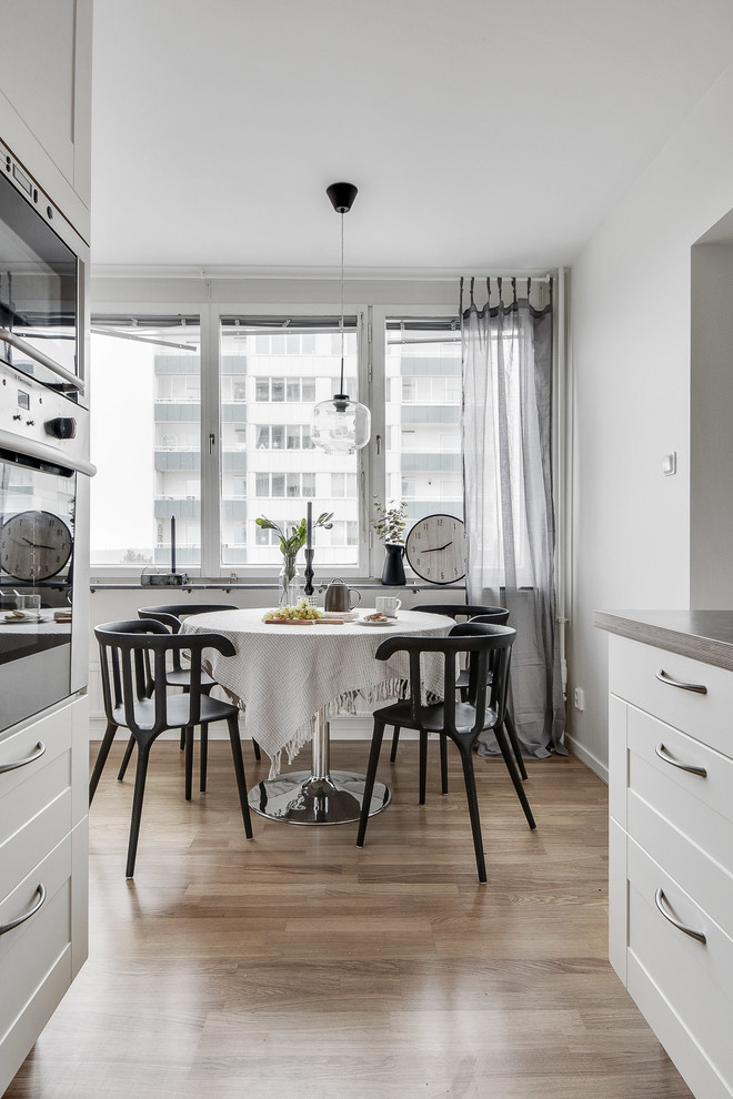 Mittelgroße Skandinavische Wohnküche ohne Kamin mit weißer Wandfarbe und braunem Holzboden in Stockholm