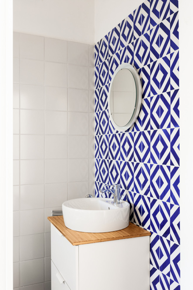 Стильный дизайн: ванная комната среднего размера в средиземноморском стиле с фасадами островного типа, белыми фасадами, душем без бортиков, раздельным унитазом, синей плиткой, керамической плиткой, белыми стенами, полом из керамической плитки, душевой кабиной, настольной раковиной, столешницей из дерева, синим полом, душем с раздвижными дверями, тумбой под одну раковину, подвесной тумбой и панелями на части стены - последний тренд